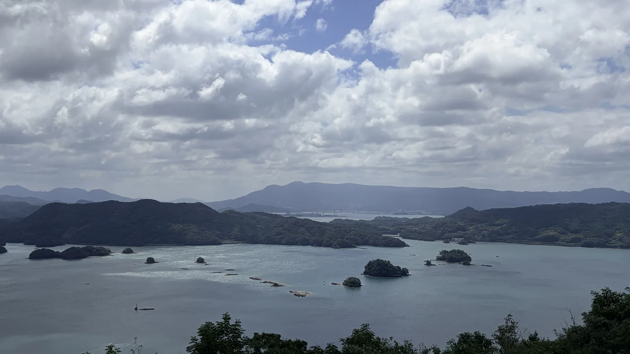 いろは島展望台から見た伊万里湾。雲の多い空の下、大小の島が湾内に点在し、奥には山並みが連なる
