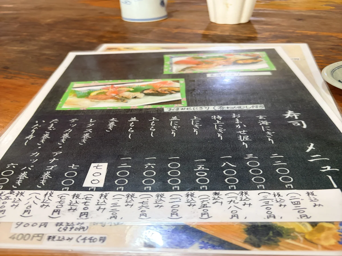 ひぜん玄海寿しの店内メニュー。黒地に手書きで寿司の品書きと価格、税込価格が並ぶ