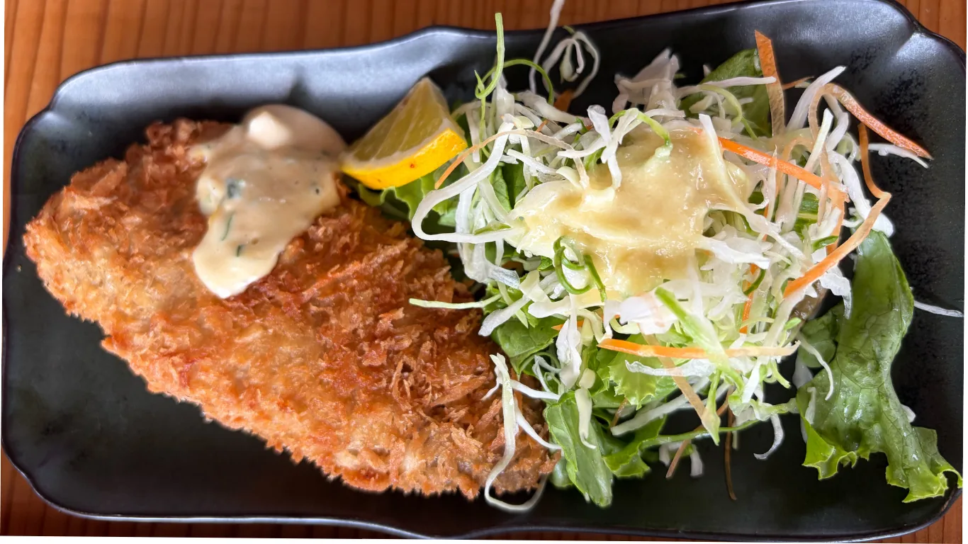 「海の見えるごはん屋」のアジフライ。粗めのパン粉で揚がった大ぶりの一枚に、タルタルソースとレモン、千切りキャベツが添えられている